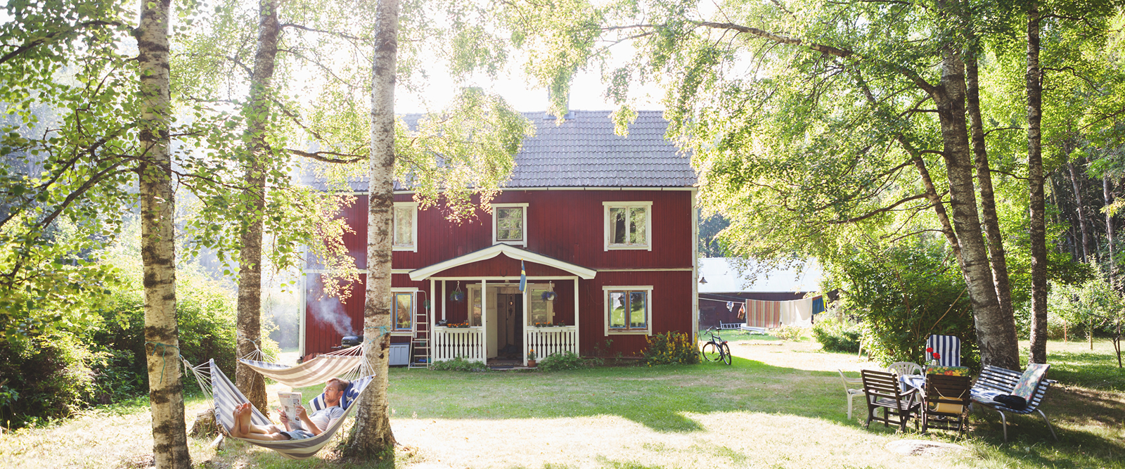 idyllic swedish cottage and summer garden with man reading in hammock